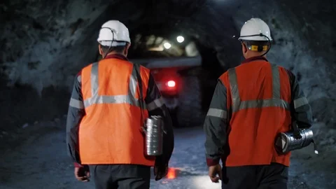 Two workers with helmets and equipment walking through a mine tunnel Stock Footage 116500616