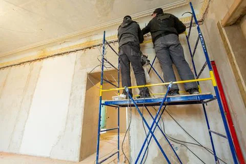 Two workers is installing the electrical wires on the wall that is the part of Stock Photos