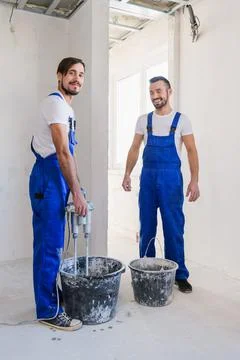Two workers knead cement with a construction mixer Stock Photos