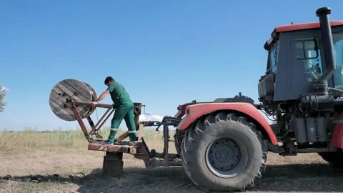 Two workers lay the cable in the ground with a large wheeled tractor Stock Footage 201959812