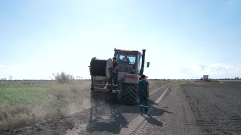 Two workers lay the cable in the ground with a large wheeled tractor Stock Footage 248524699