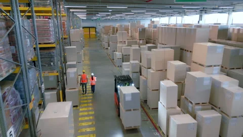 Two workers in orange vests navigate a warehouse aisle. 库存影片 307996926