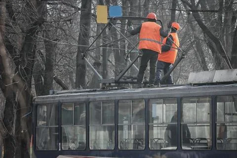 Two workers in orange vests repair the contact network on the roof of a tra.. Stock Photos