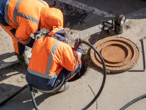 Two workers over the open sewer hatch on a street Stock Photos