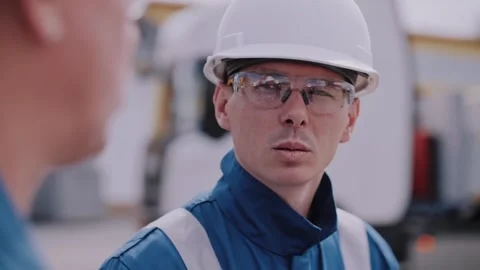 Two workers in overalls are talking. A truck passes by in the background. Stock Footage 316320813