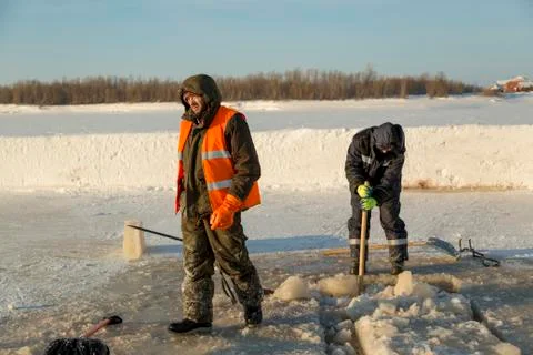 Two workers in overalls remove ice from the hole 스톡 사진