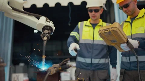 Two workers in safety gear observe a welding robot Stock Footage 344920571