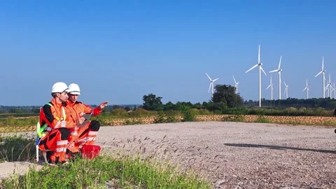 Two workers in safety gear survey a wind farm site under a clear blue sky 스톡 동영상 330041787