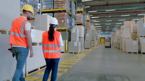 Two workers in safety vests navigate a warehouse aisle. 動画素材 308003049