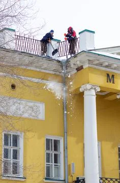 Two workers with a shovel and scraper remove the snow from the roof Stock Photos