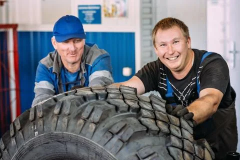 Two Workers Smiling While Handling Large Tire in Garage Stock Photos