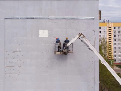 Two workers stand on aerial platform and insulate the wall of the house Stock Photos