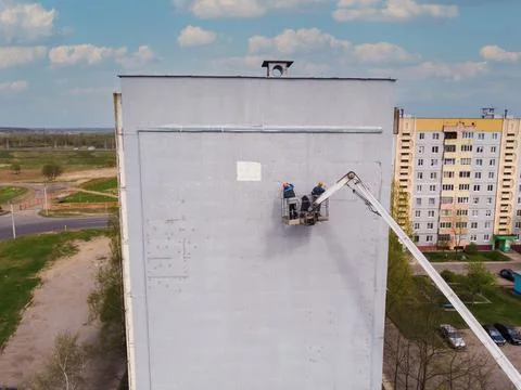 Two workers stand on an aerial platform and repair the wall of a house. Top view Stock Photos