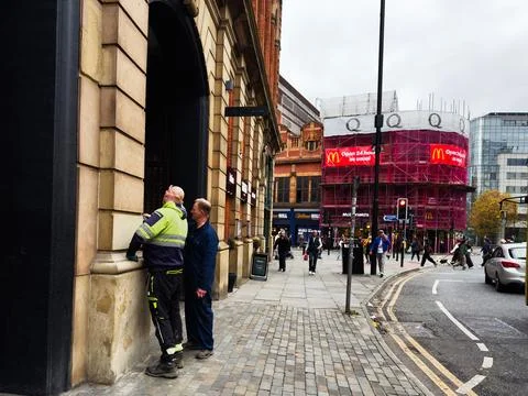 Two workers talk outside a historic Manchester building as a busy city stre.. Fotos de archivo
