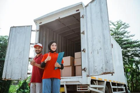 Two workers with thumbs up standing behind a logistics container Stock Photos