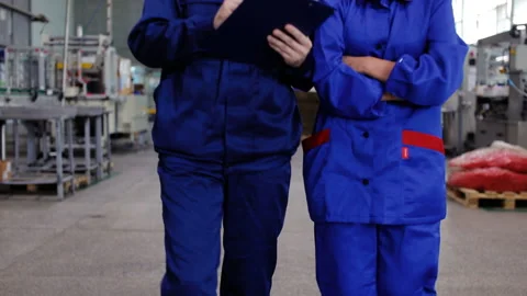 Two workers in uniform in a factory discuss Stock Footage 95734634