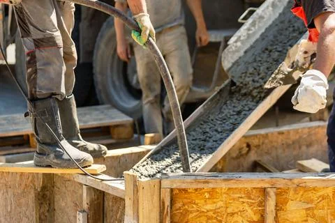 Two workers use hoses to pour concrete into a wooden structure at a construct Stock Photos
