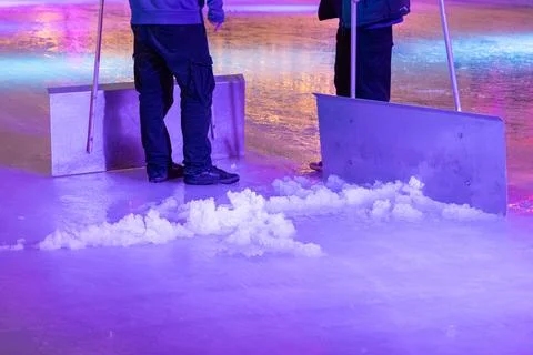 Two workers using large metal scrapers to clear white snow piles from a smooth Stock Photos