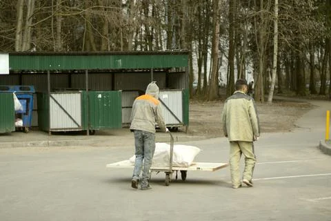 Two workers in work clothes carry garbage to the garbage on a cart. Cloudy da Foto stock