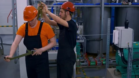 Two workers at work in hard hats at the factory put on rescue belt for work in a Stock Footage 168924925