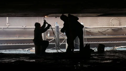Two workers work under the ship, the welder cooks metal on the bottom Stock Footage 87320321