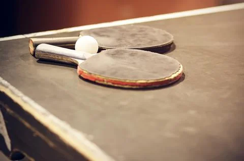 Two worn red and gray ping-pong rackets and a white plastic ball lie on an ol Stock Photos