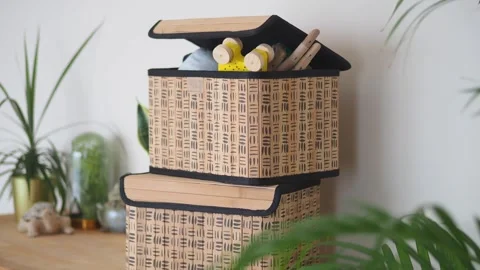 Two woven storage boxes stacked on wooden shelf in bright room with green p.. Stock Footage 332144070