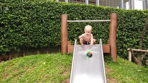 A two-year blond boy plays with a baby car on a children's slide, the car rolls  Stock Footage 104749919