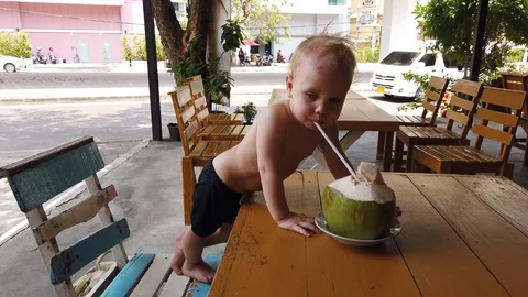 Two-year-old blond boy with a serious face drinking coconut with a straw. Stock Footage 104848586