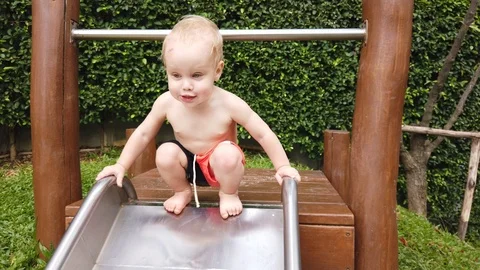 Two-year-old blond boy with great joy and fun down the hill on the Playground. Stock Footage 104848845