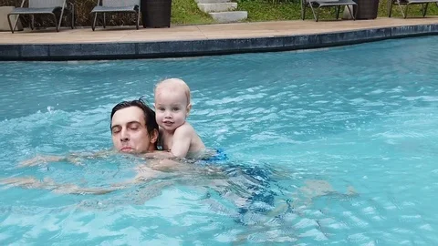 A two-year-old blond boy sits on his father's back and they swim together in the Stock Footage 104849180