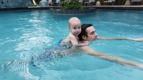 A two-year-old blond boy sits on his father's back and they swim together in the Stock Footage 104849256