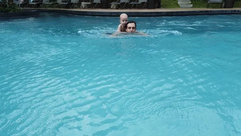 A two-year-old blond boy sits on his father's back and they swim together in the Stock Footage 104849326