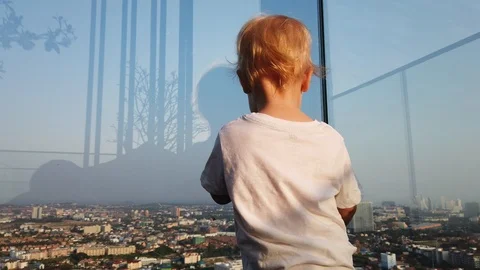 A two-year-old blond boy looks down at the city through the glass, Stock Footage 105052546