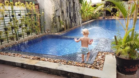 A two-year-old blond boy awkwardly enters the pool, holds a baby car in his hand Stock Footage 105708951