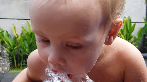 Two-year-old blond boy Sunny summer day drinking from a garden hose Stock Footage 107965311