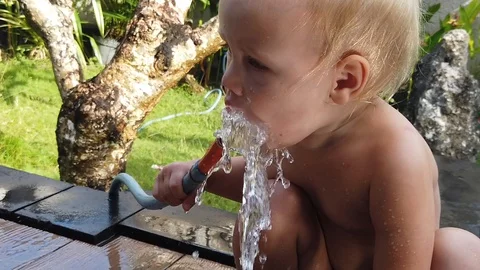 Two-year-old blond boy Sunny summer day drinking from a garden hose Vidéo 107965409