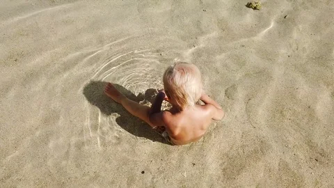 A two-year-old blond boy sits in clean sea water and plays with children's toys. Vidéo 108577818