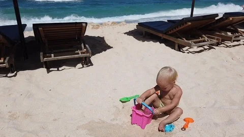 Two-year-old blond boy playing with sand on the beach. Vidéo 108578264