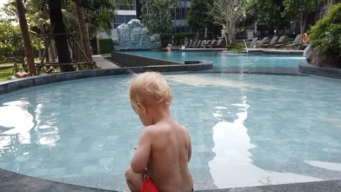 A two-year-old blond child plays with a toy, being hardly with a pool.  Stock Footage 104701943