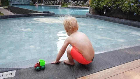 A two-year-old blond child plays with a toy, being hardly with a pool.  Stock Footage 104702189