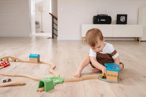 A two-year-old boy in a brown overall and white T-shirt plays with toys at home Stock Photos