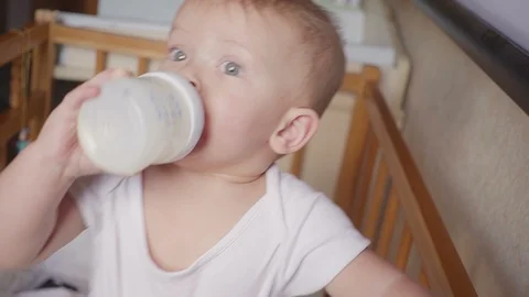 Two year old boy drinking milk from plastic bottle in his bed looking up Video stock 90344708