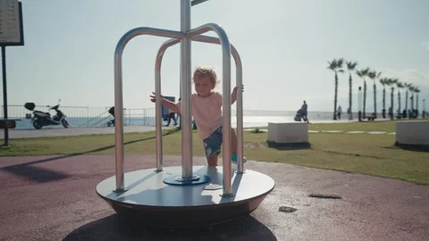Two-year-old boy kid in the spring on the playground rides on the carousel Stock Footage 244875648