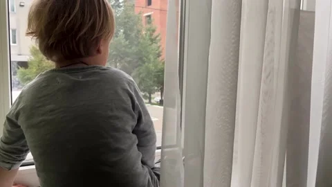 A two-year-old boy sits and looks out the window at passing cars. Alone Stock Footage 190624424