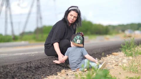 A two-year-old child and his mother are sitting by the side of the highway Stock Footage 245656240