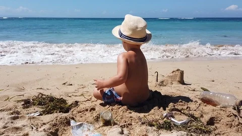 Two-year-old child in a beach hat playing on the beach with garbage Stock Footage 108719753