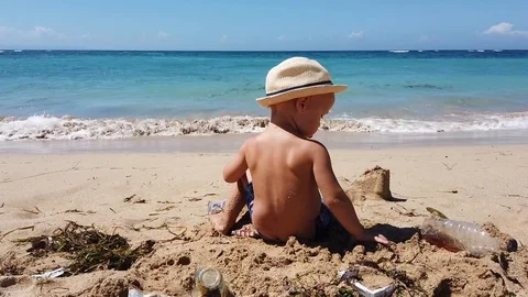 Two-year-old child in a beach hat playing on the beach with garbage Vidéo 108719776