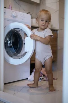Two year old child doing household chores. Loading washing machine. Stock Photos