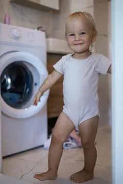 Two year old child doing household chores. Loading washing machine. Stock Photos